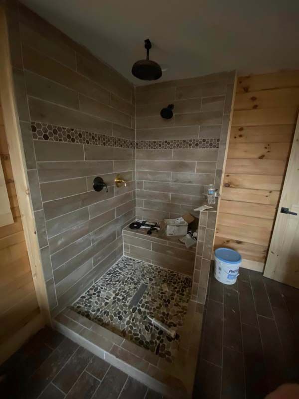 Shower with wood-look tile, pebble floor, and dark fixtures in a room with wood paneling.