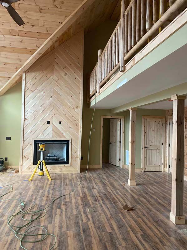 Interior of a house under construction; fireplace with chevron wood paneling, wood flooring, and a loft.
