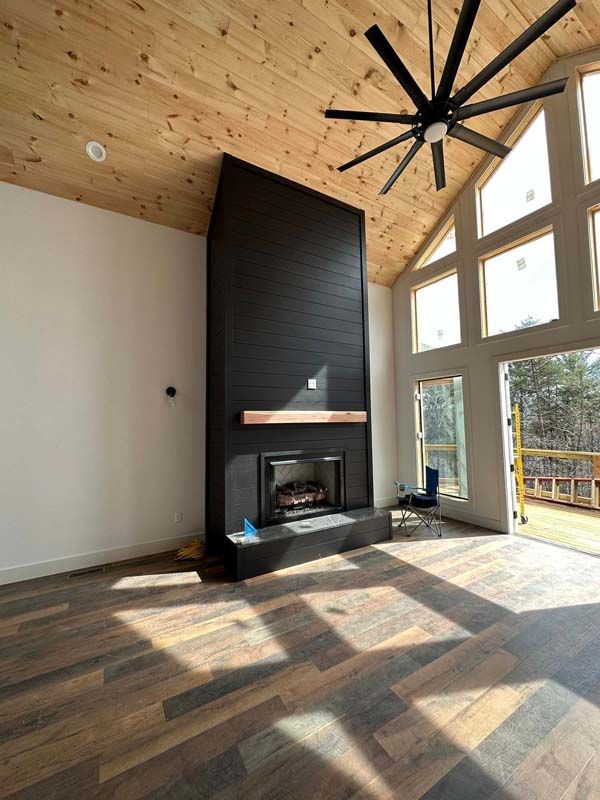 Modern living room with black fireplace, wood ceiling, and large windows.