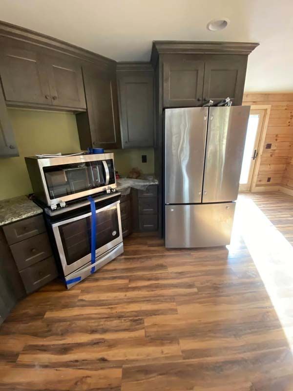 Kitchen with grey cabinets, stainless steel appliances, and wood-look flooring. New oven and microwave are in place.