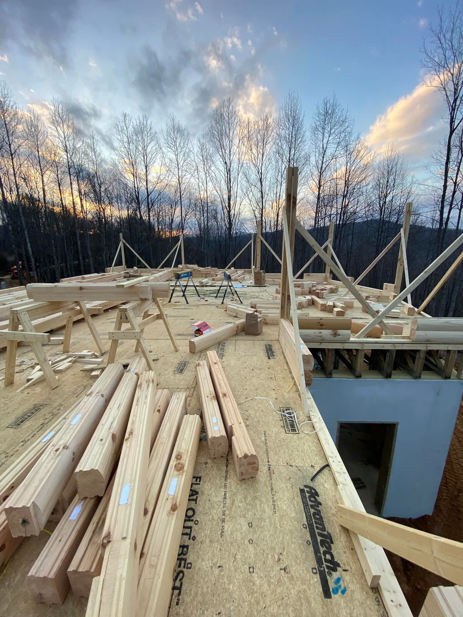 Construction site with exposed wooden framing and plywood under an evening sky.