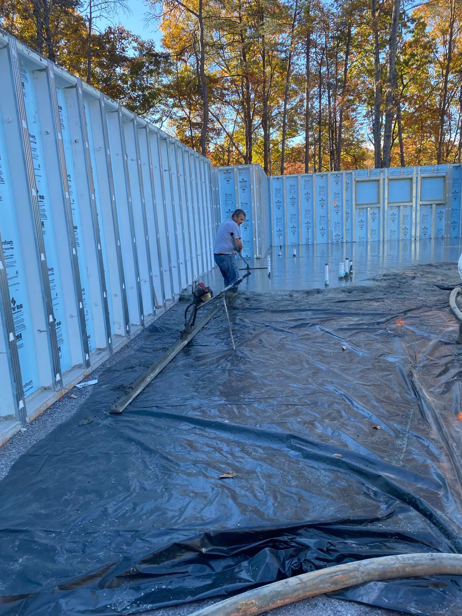 Man smoothing concrete inside a partially constructed building. Walls are lined with blue insulation.