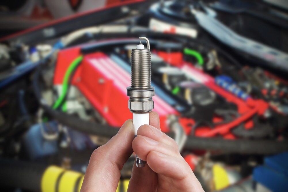 A Person is Holding a Spark Plug in Front of a Car Engine — Innisfail Auto Electrics Pty Ltd in Tully, QLD