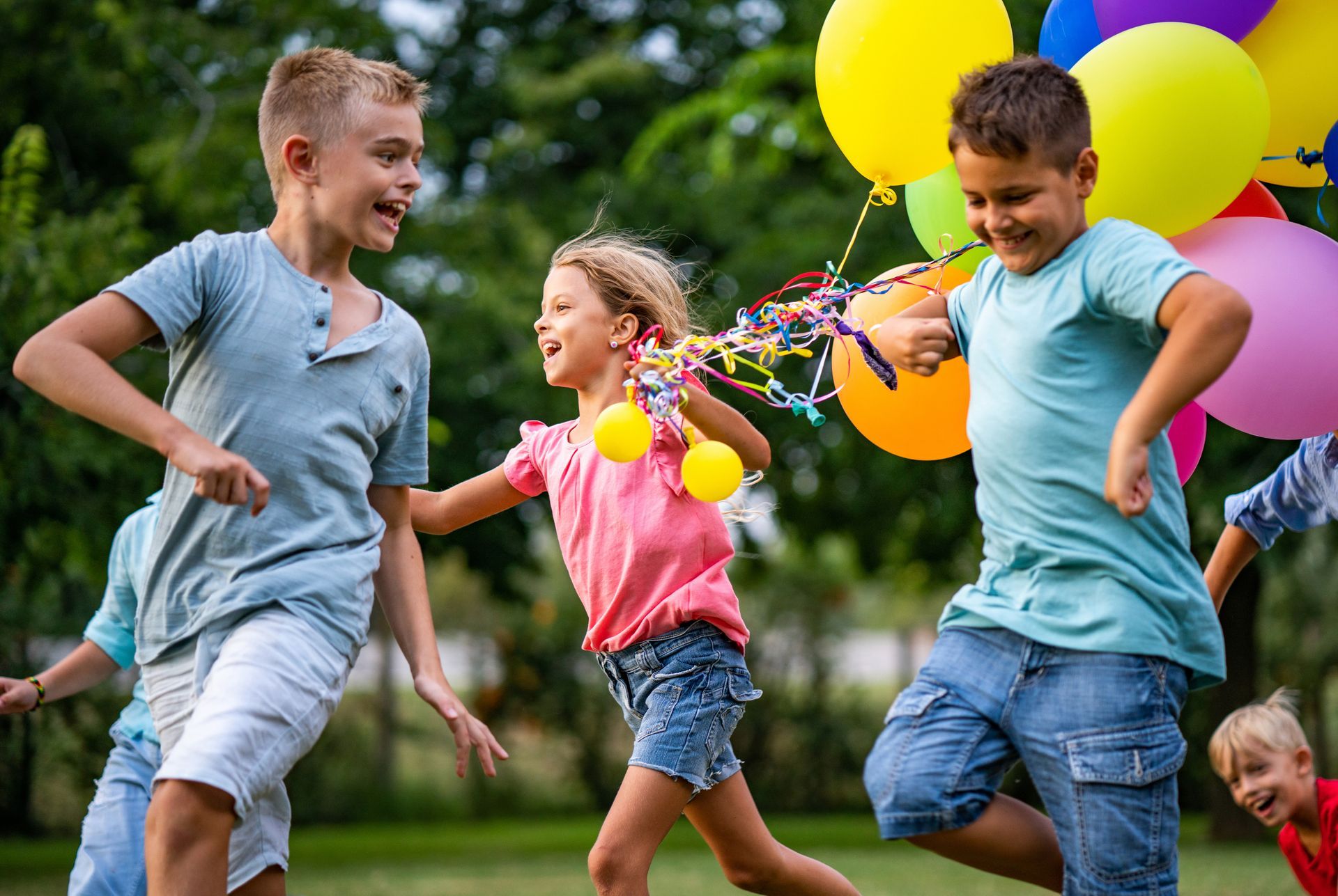 Children running with balloons in a grassy park, smiling and playing together.