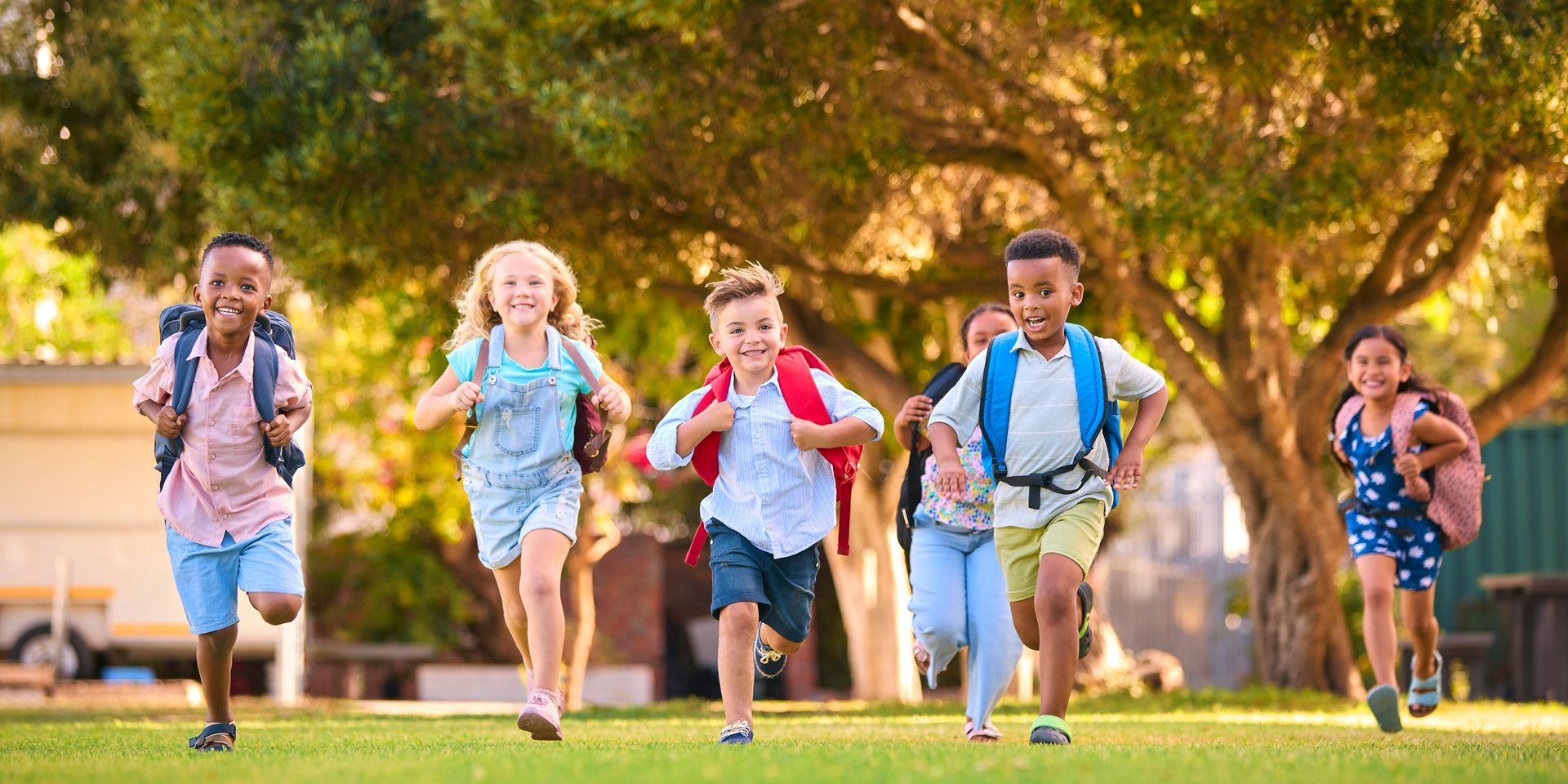 Children running with backpacks in a sunny park, smiling and playing together