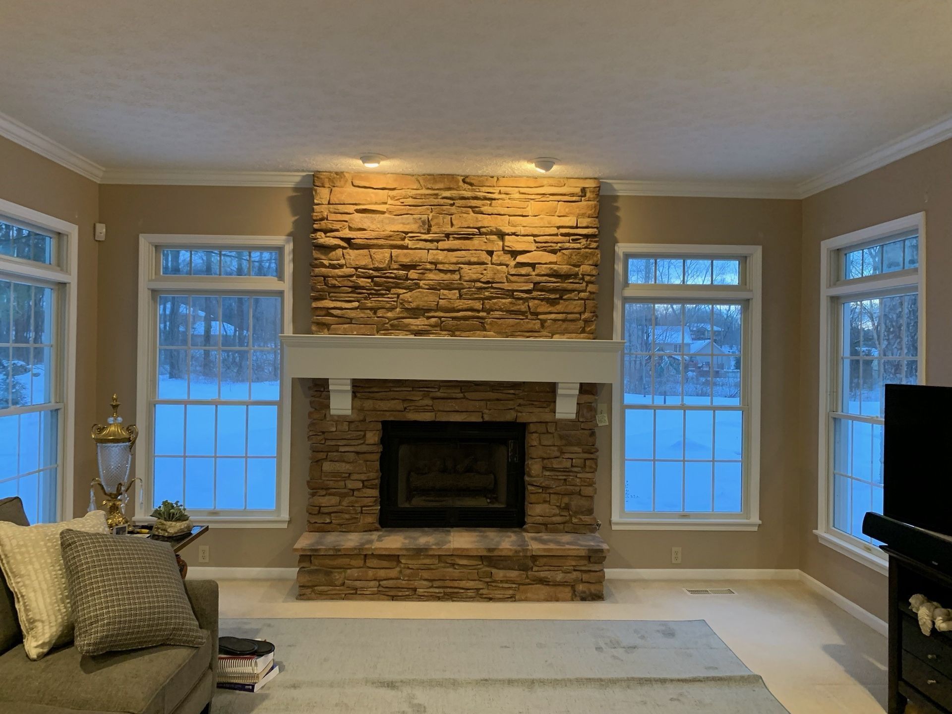Living room with a stone fireplace, flanked by windows looking out at snow.