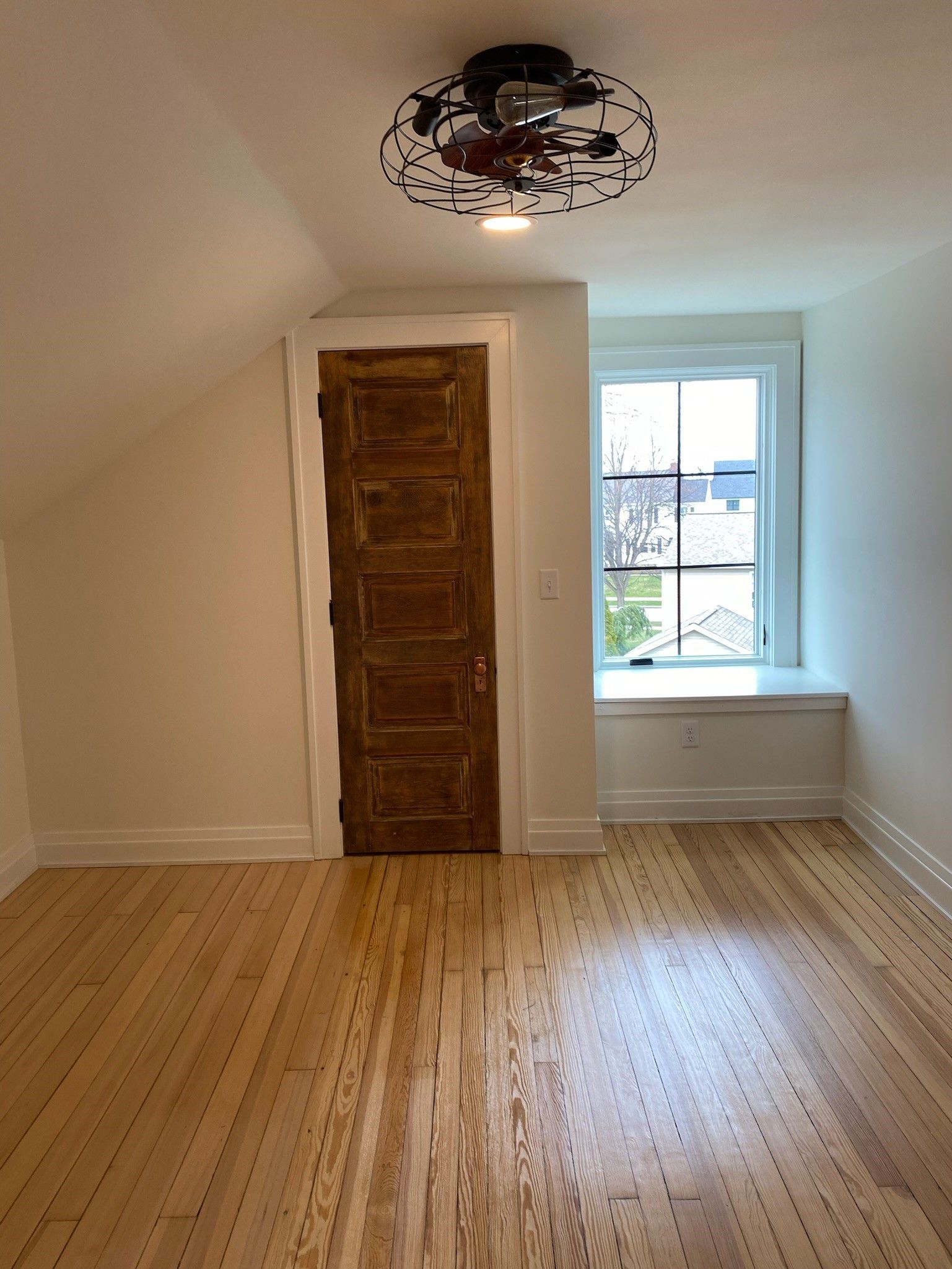 Room with wood floor, brown door, small window with a white seat, and a disco ball ceiling light.