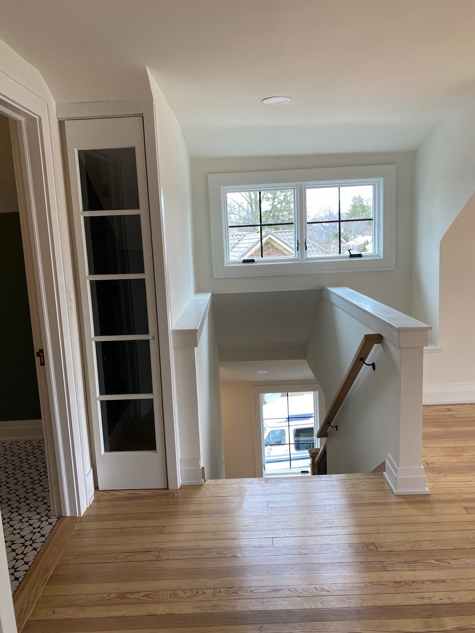 Hallway with wooden floor, staircase, and window. White walls, and light filtering through.