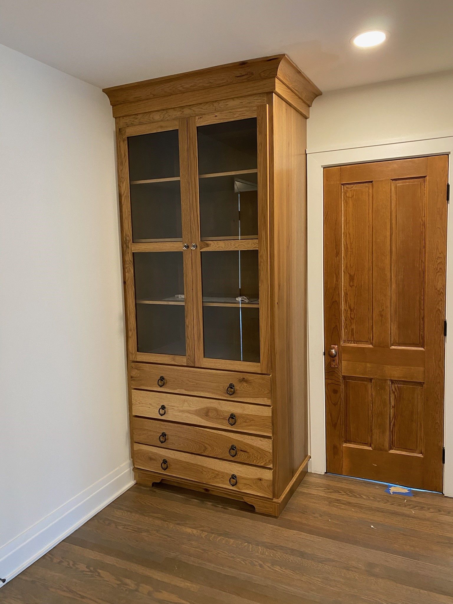 Wooden cabinet with glass doors and drawers next to a wooden door. Light brown walls and floor.