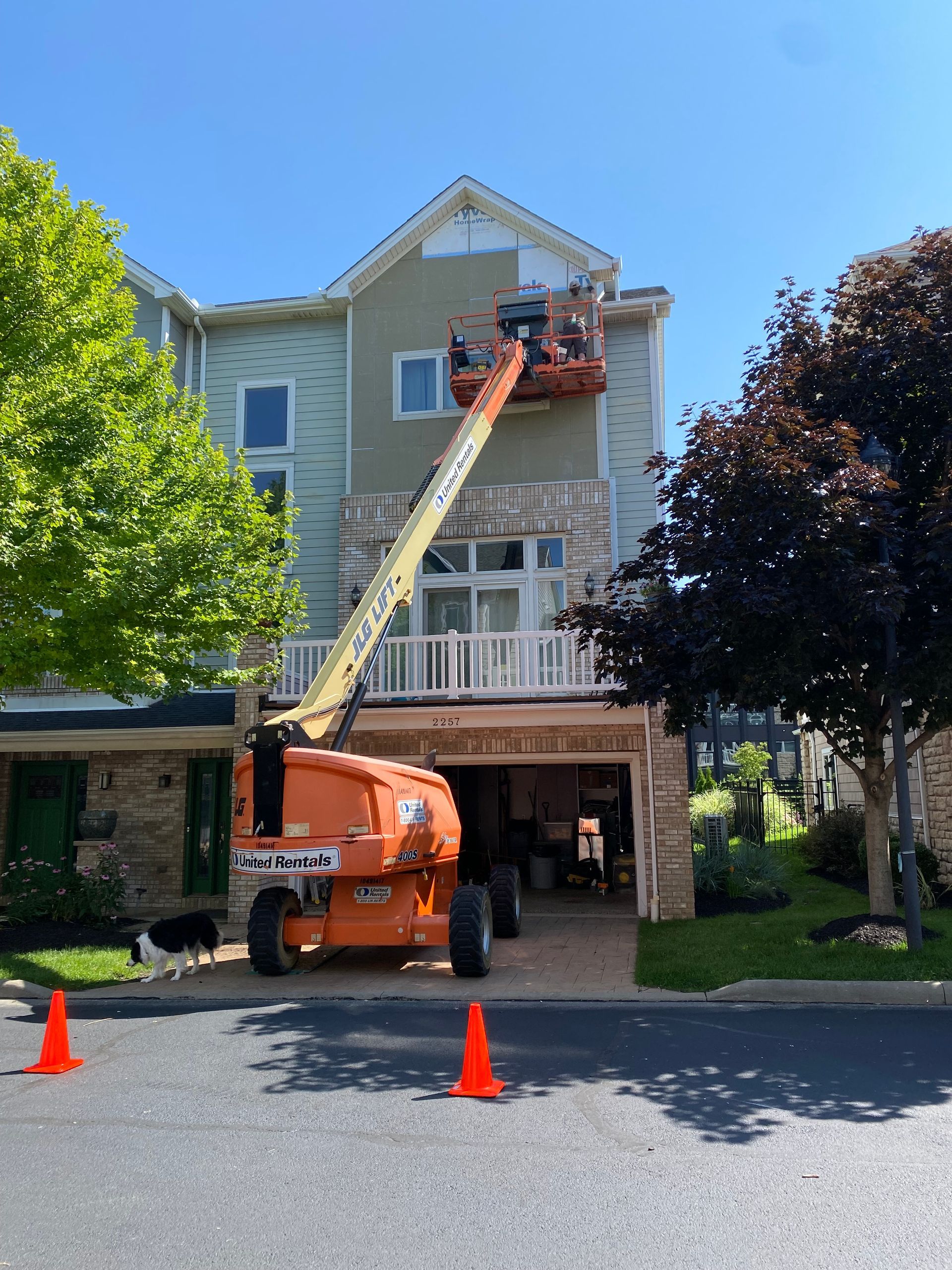 A lift platform with a worker is painting the exterior of a multi-story building on a sunny day.