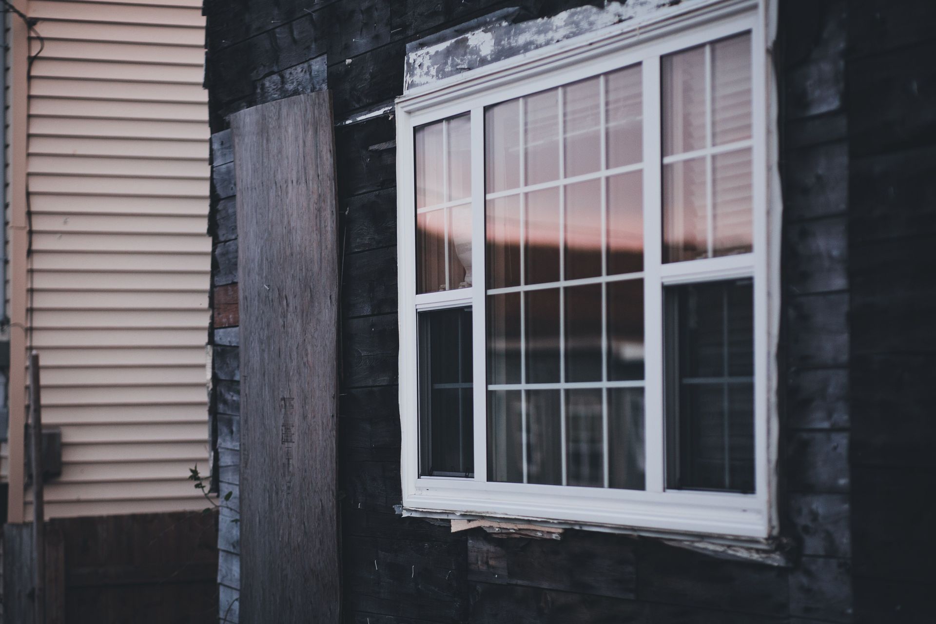 White-framed window on a dark house wall beside beige siding at sunset