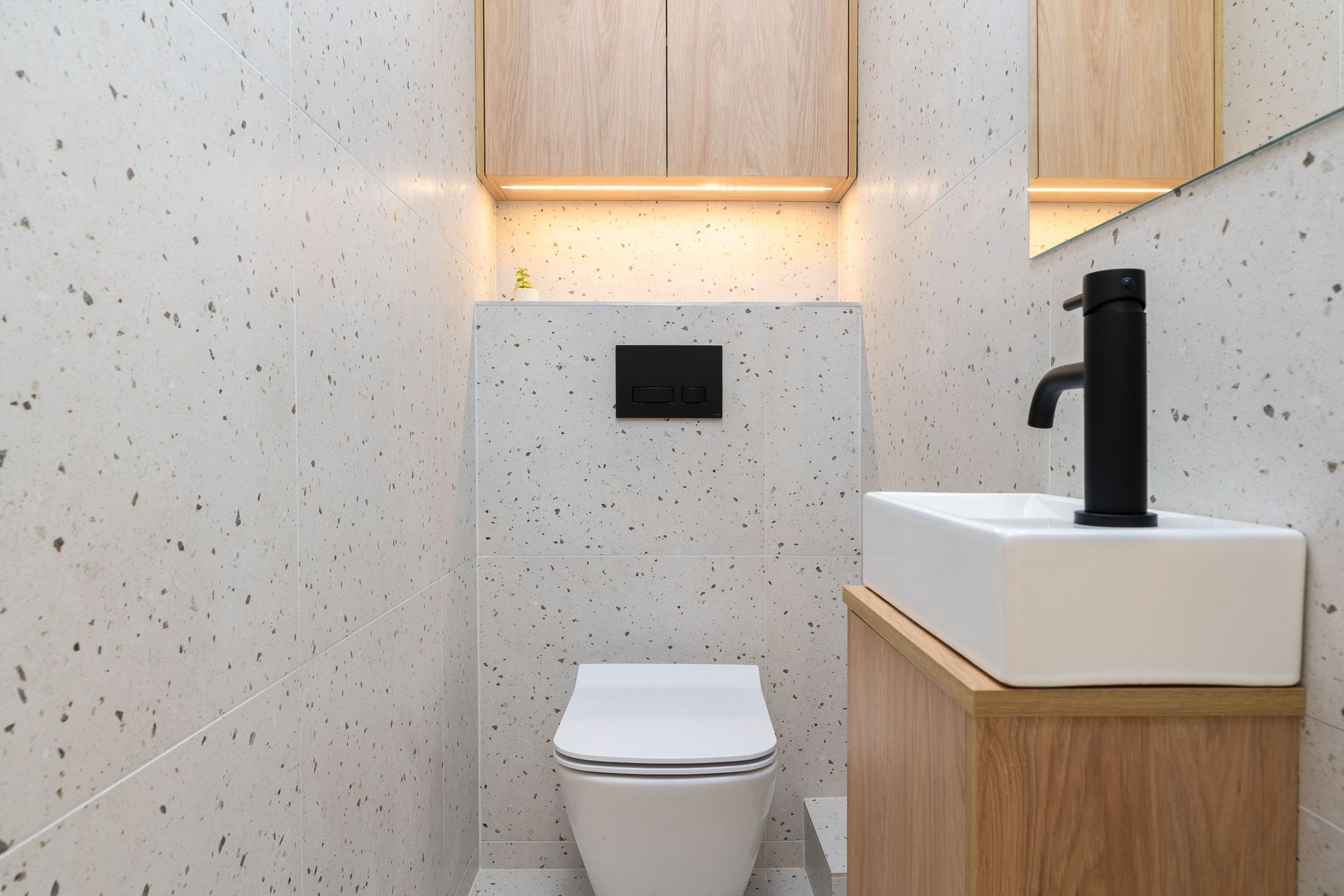 Modern white bathroom with toilet, sink, black faucet, and wood cabinetry.