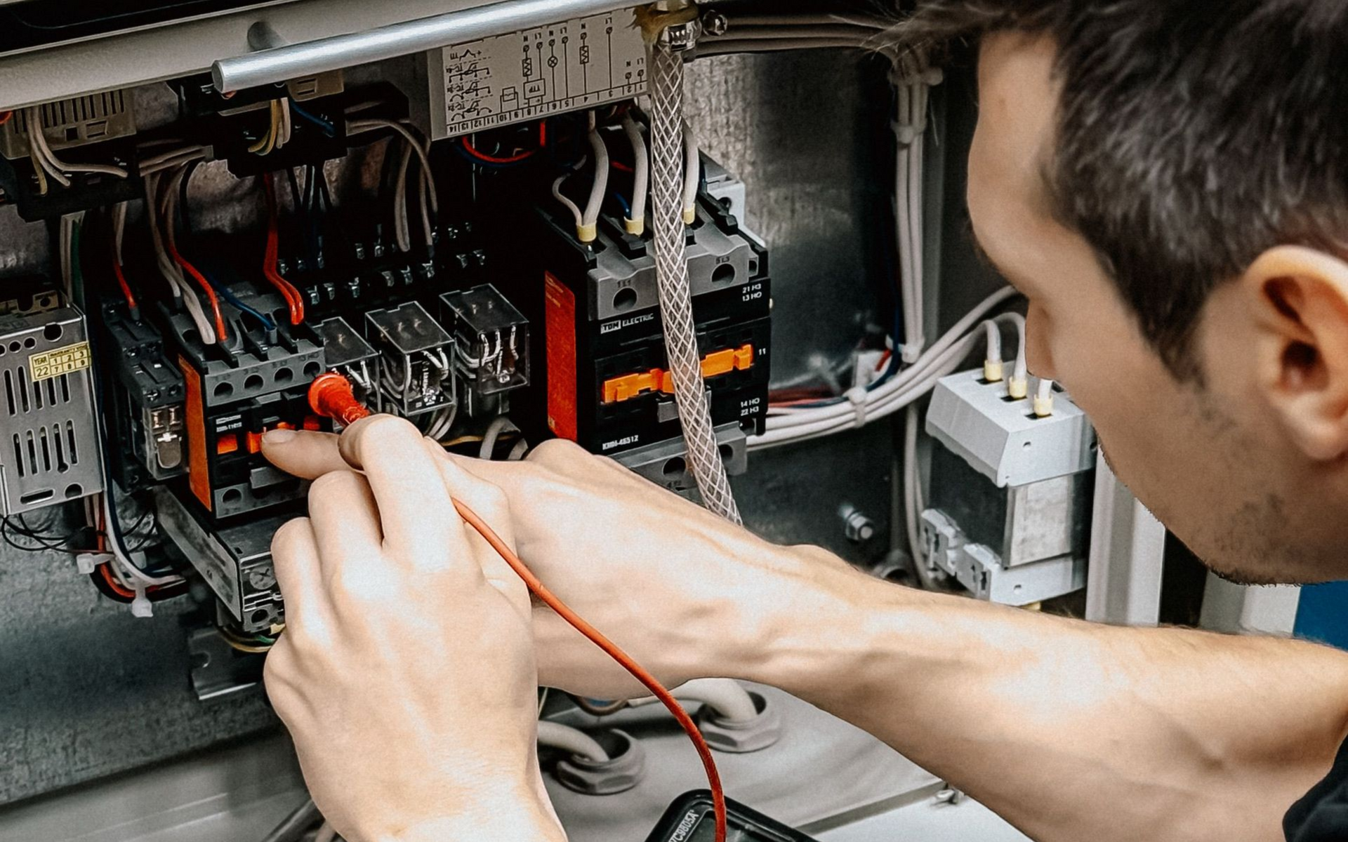 Technician using a screwdriver to repair an electrical panel with wires and circuit breakers