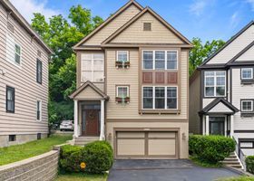 Tan beige two-story townhouse with garage, front steps, and small shrubs on a quiet street