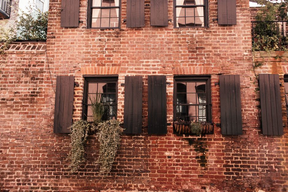 Brick building facade with dark shutters and a small balcony, covered in ivy.