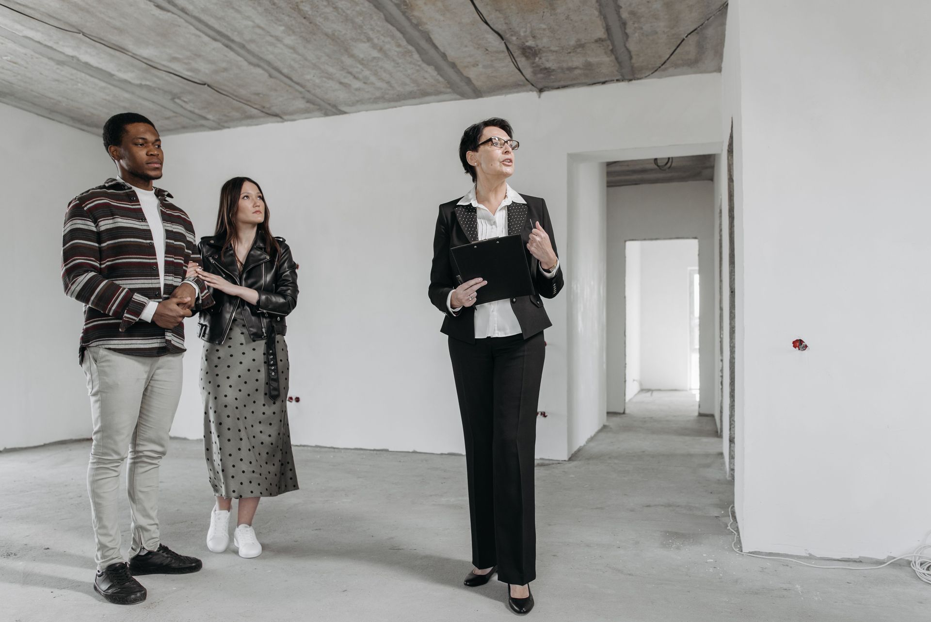 Three people standing in an unfinished room, looking around and discussing the space.