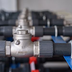 Two red industrial valves on a silver pipe against a concrete wall in a utility room