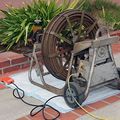 Technician kneels on tiled floor, repairing a drain near a spinning floor machine and red extension cord.