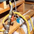 Technician inspecting copper pipes and boiler connections under a sink, using a wrench and flashlight