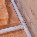 Exposed underground plumbing with black pipes and a blue-capped vertical pipe in a dirt trench