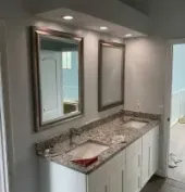 Bathroom with dual sinks, mirrors, and granite countertop; white cabinetry; light blue walls.