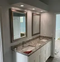 Bathroom with dual sinks, mirrors, and granite countertop; white cabinetry; light blue walls.
