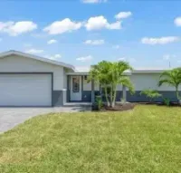 A single-story house with a grey garage door, white walls, and a green lawn under a blue sky.
