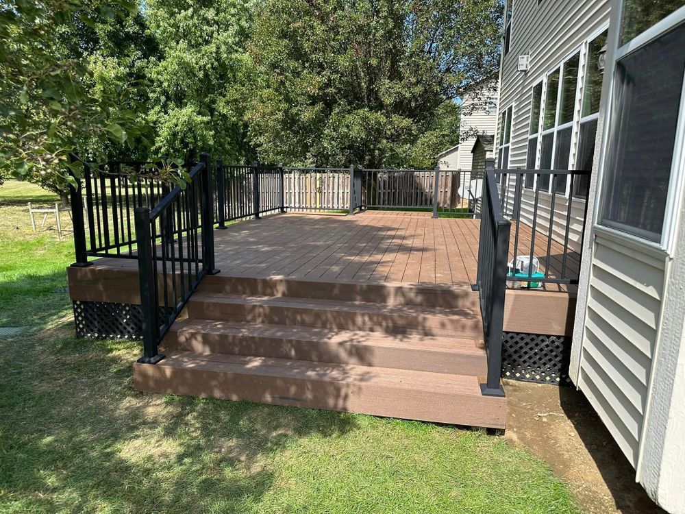 A composite deck with black railing and steps on a grassy lawn.