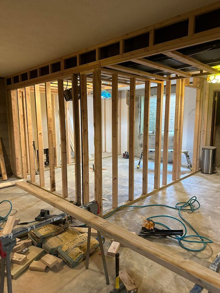 Interior view of a room under construction; wood framing of new walls, tools, and building materials.