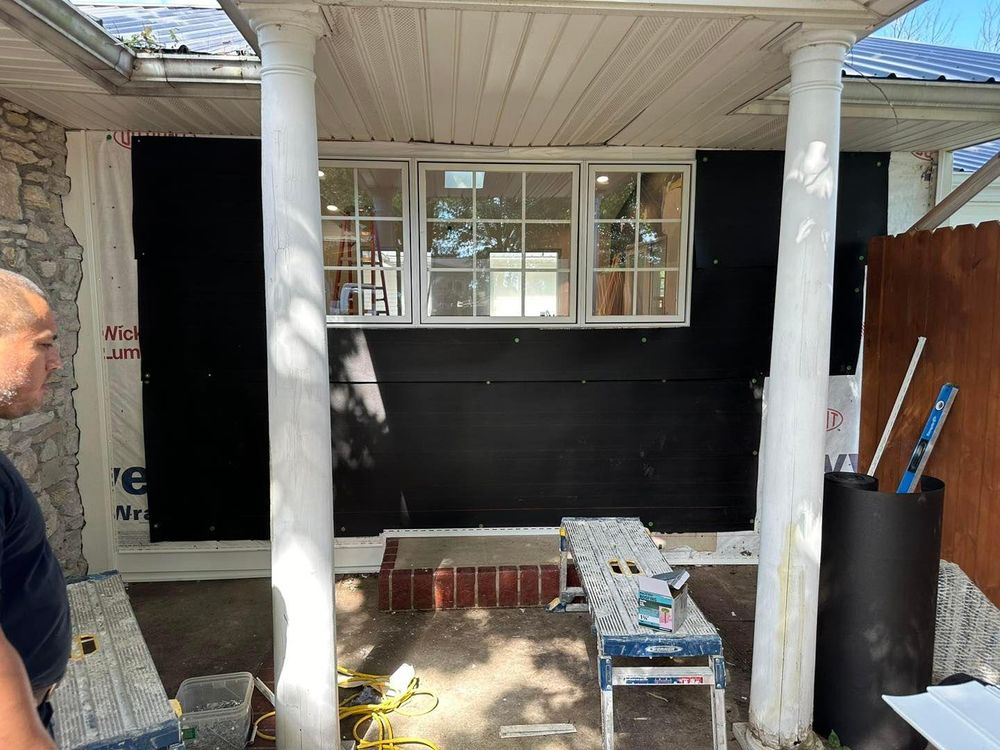 Construction site: Exterior wall with windows, covered in black material, between two white columns.