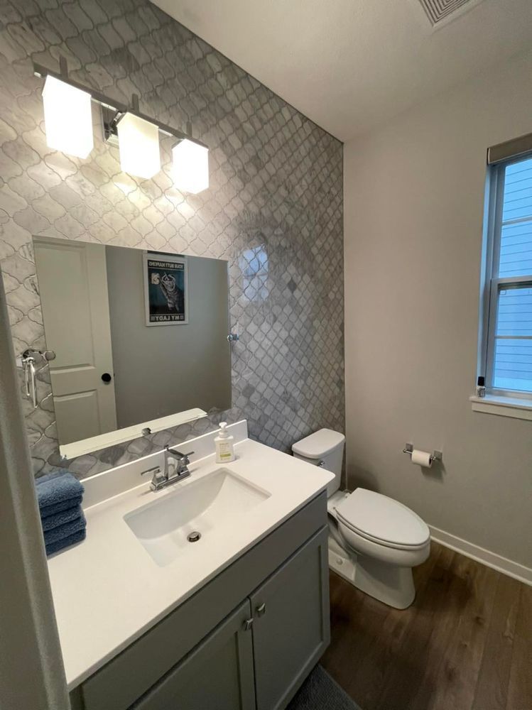 Bathroom with gray vanity, patterned tile wall, toilet, and window.