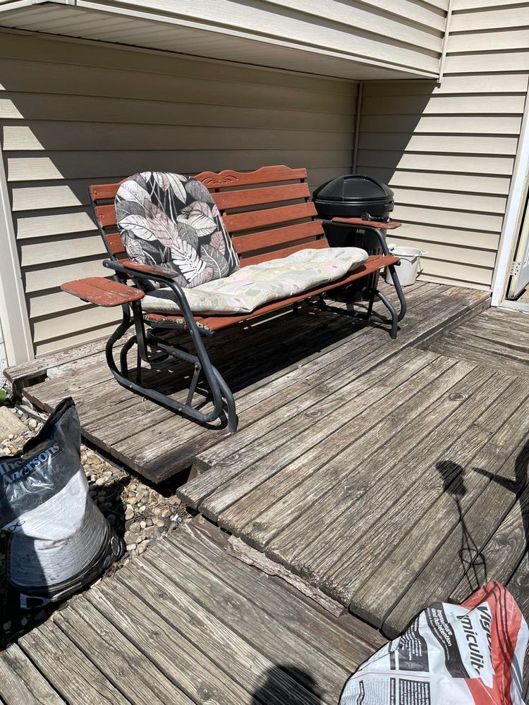 Outdoor bench on a wooden deck, with cushions and small charcoal grill.