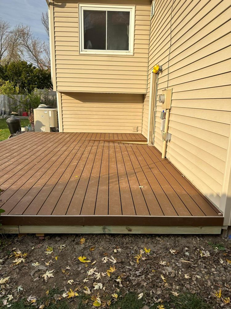 Brown composite deck attached to a beige house. The deck sits on the ground with fallen leaves.