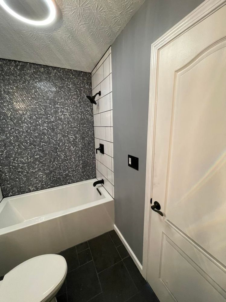 Bathroom with black and white tile, white tub, grey wall, and closed white door.