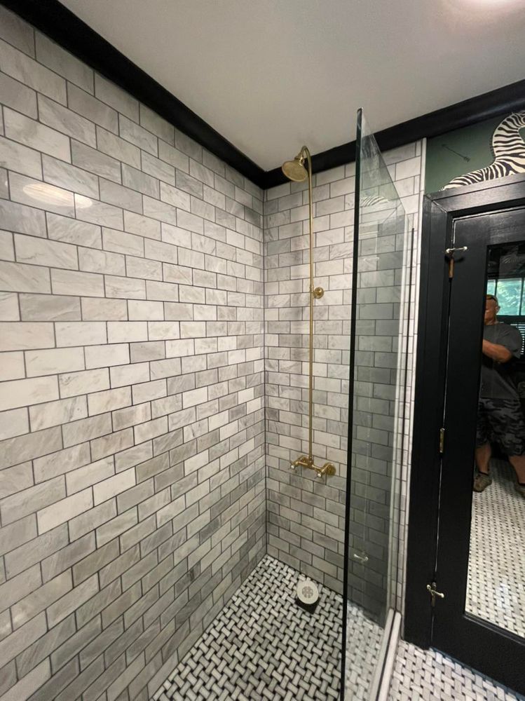 Shower with white brick tiles and gold fixtures. Glass door, black trim, and black and white floor.