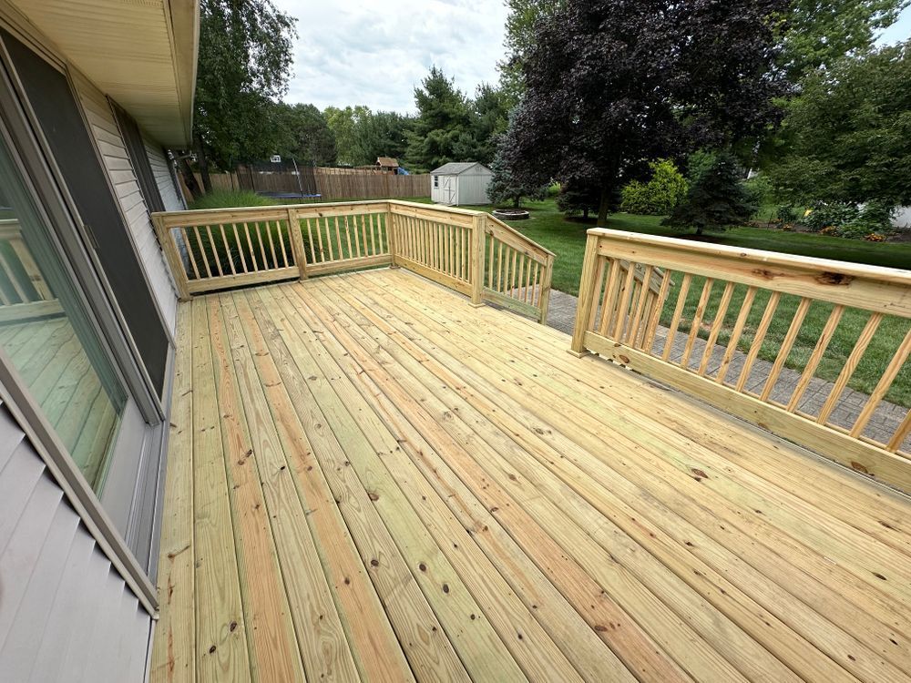 Wooden deck with railing next to a house, view of yard with trees and grass.