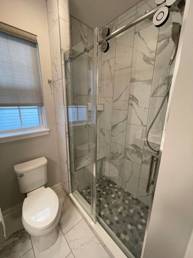 Small bathroom with toilet, shower with sliding glass door, and window.