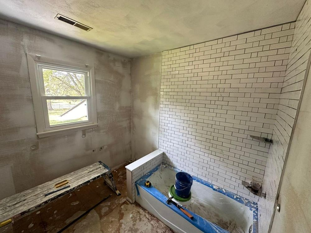 Bathroom remodel in progress: partially tiled walls, tub, window, tools, and unfinished surfaces.