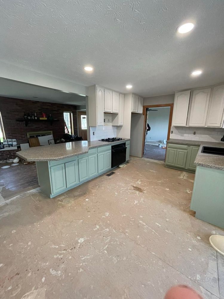 Kitchen renovation in progress: white and seafoam cabinets, granite counters, unfinished floor.