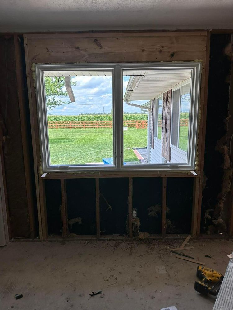 Window in a room under construction with wooden trim, showing a view of a yard.