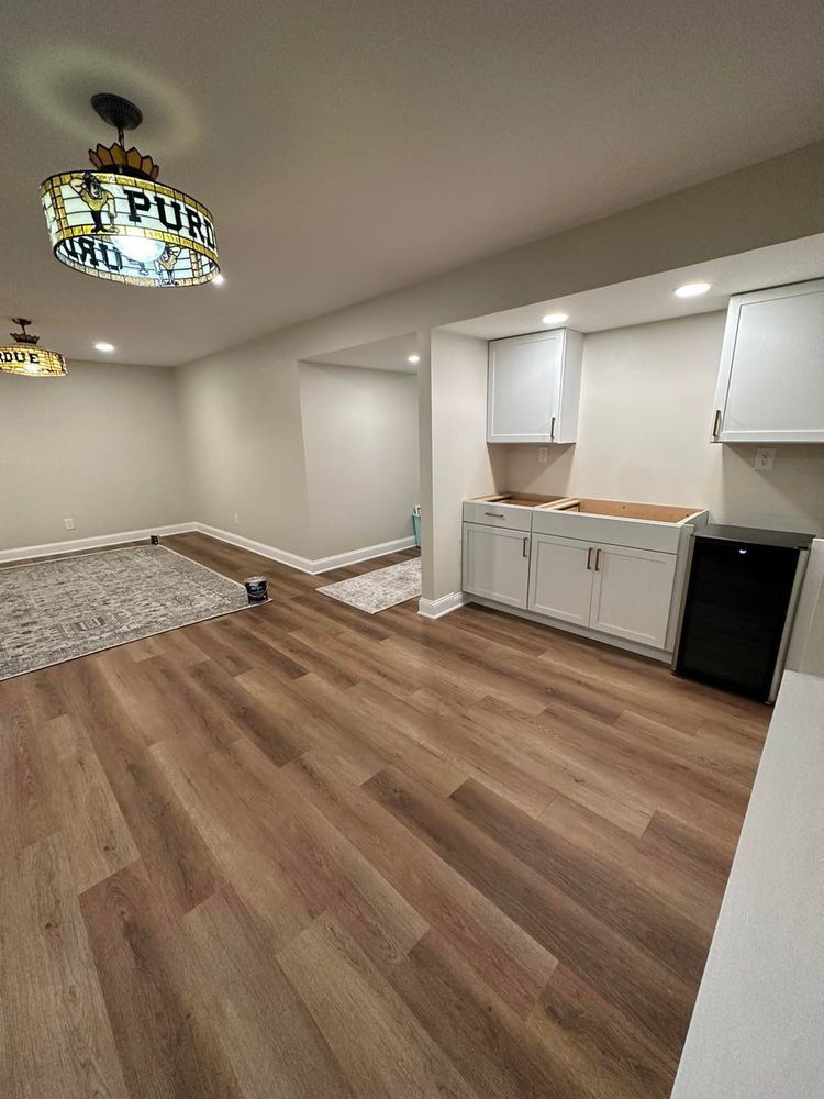 A finished basement with new wood flooring, white cabinets, and a pub-themed light fixture.