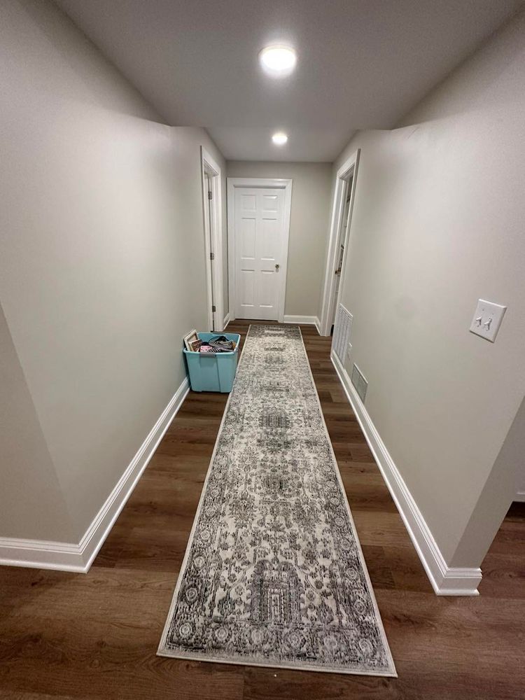 Long hallway with brown flooring, grey walls, white trim, and a patterned runner rug.
