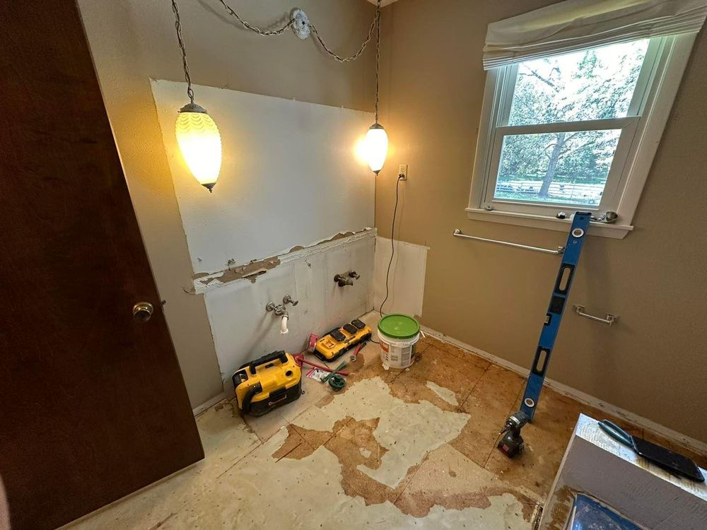 Bathroom under renovation, exposed wall and flooring. Tools and lights visible.