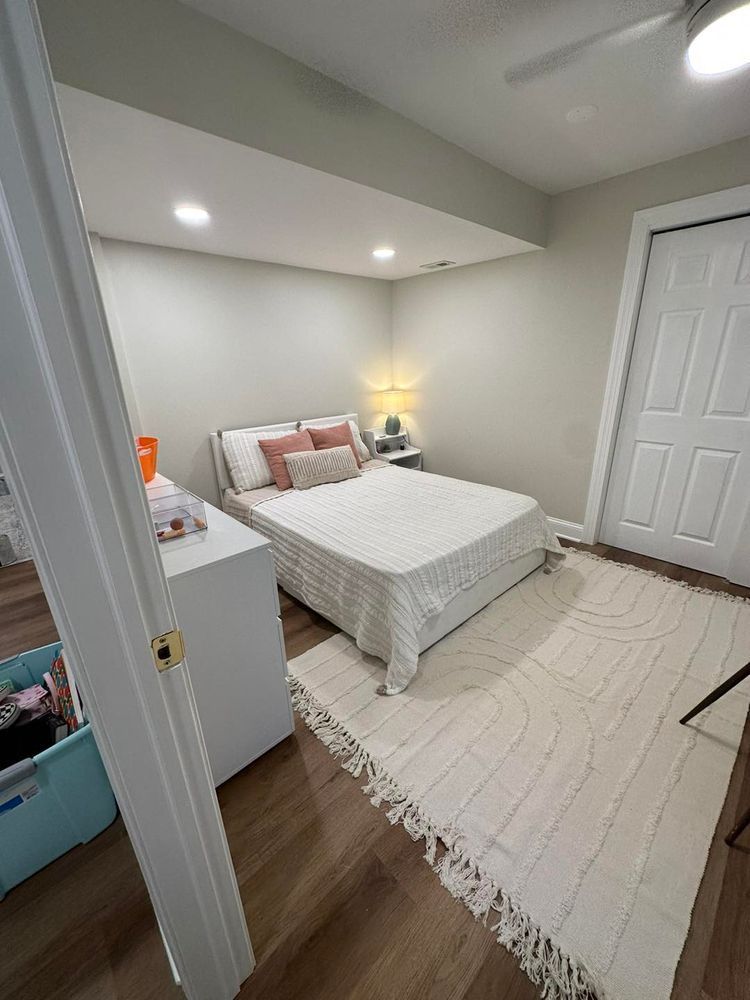 Cozy bedroom with a bed, rug, dresser, and door. Neutral colors with a warm, inviting atmosphere.