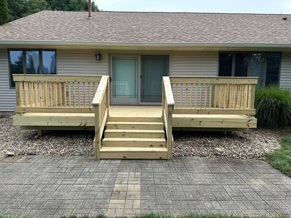 Wooden deck with stairs leading to a sliding glass door. Deck has railings and is built on a gravel base.