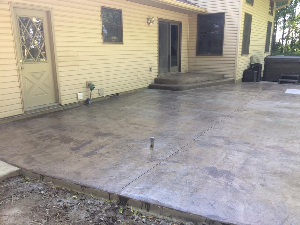 Concrete patio outside a beige house with a door, windows, and a hot tub.