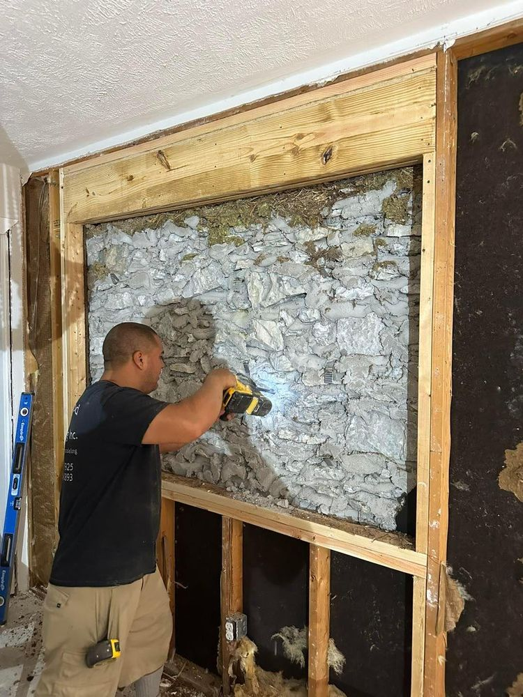 Man using a drill on a stone wall framed with wood. Construction is ongoing.