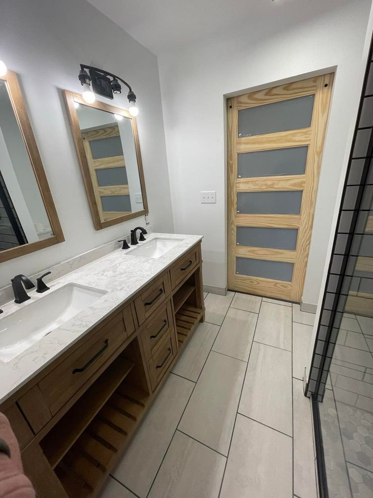 Bathroom with double vanity, light wood door with glass panels, and tiled floor.