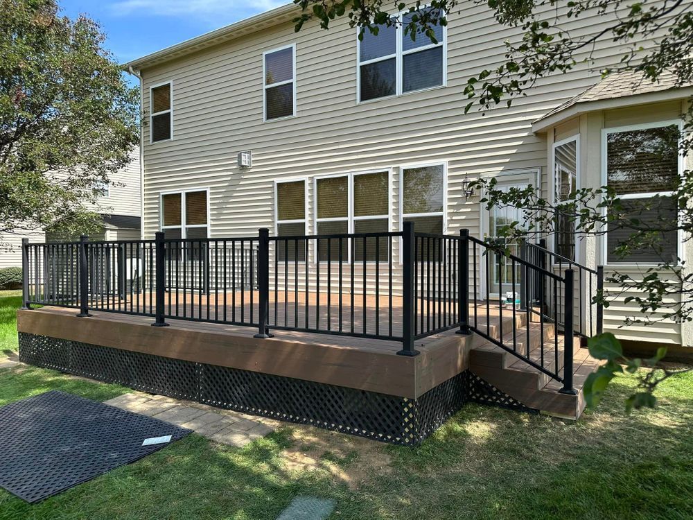 Black railing deck with brown deck boards, attached to a beige house with large windows, and a green lawn.