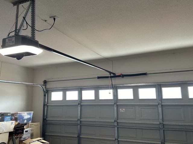 A garage door opener is hanging from the ceiling above a garage door.